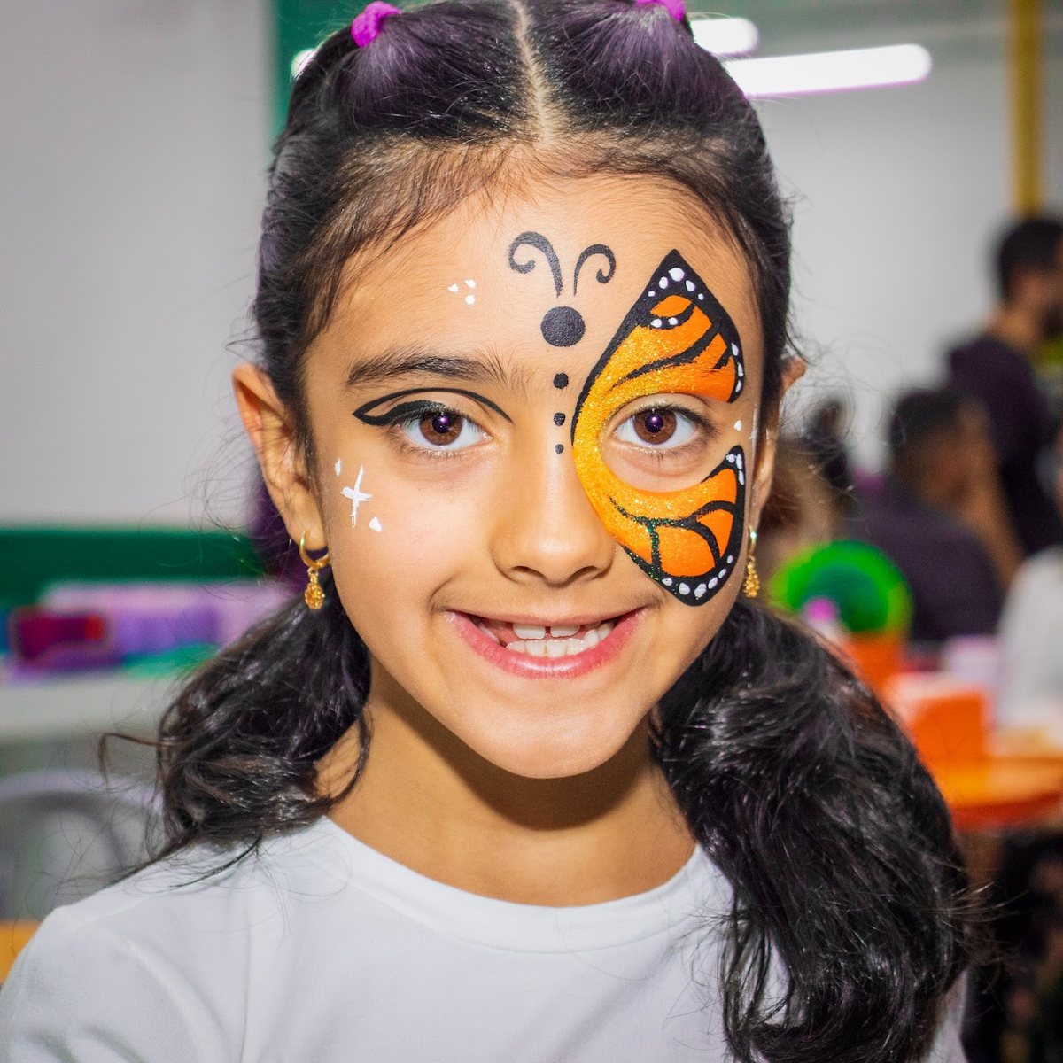 Menina sorrindo com pintura de borboleta laranja no rosto, numa festa infantil
