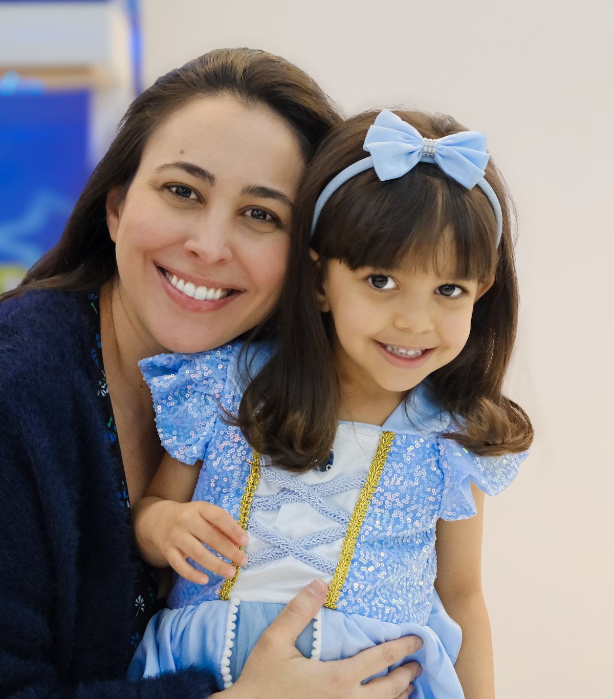 Mãe abraçando a filha vestida de Cinderela, as duas sorrindo, numa festa infantil