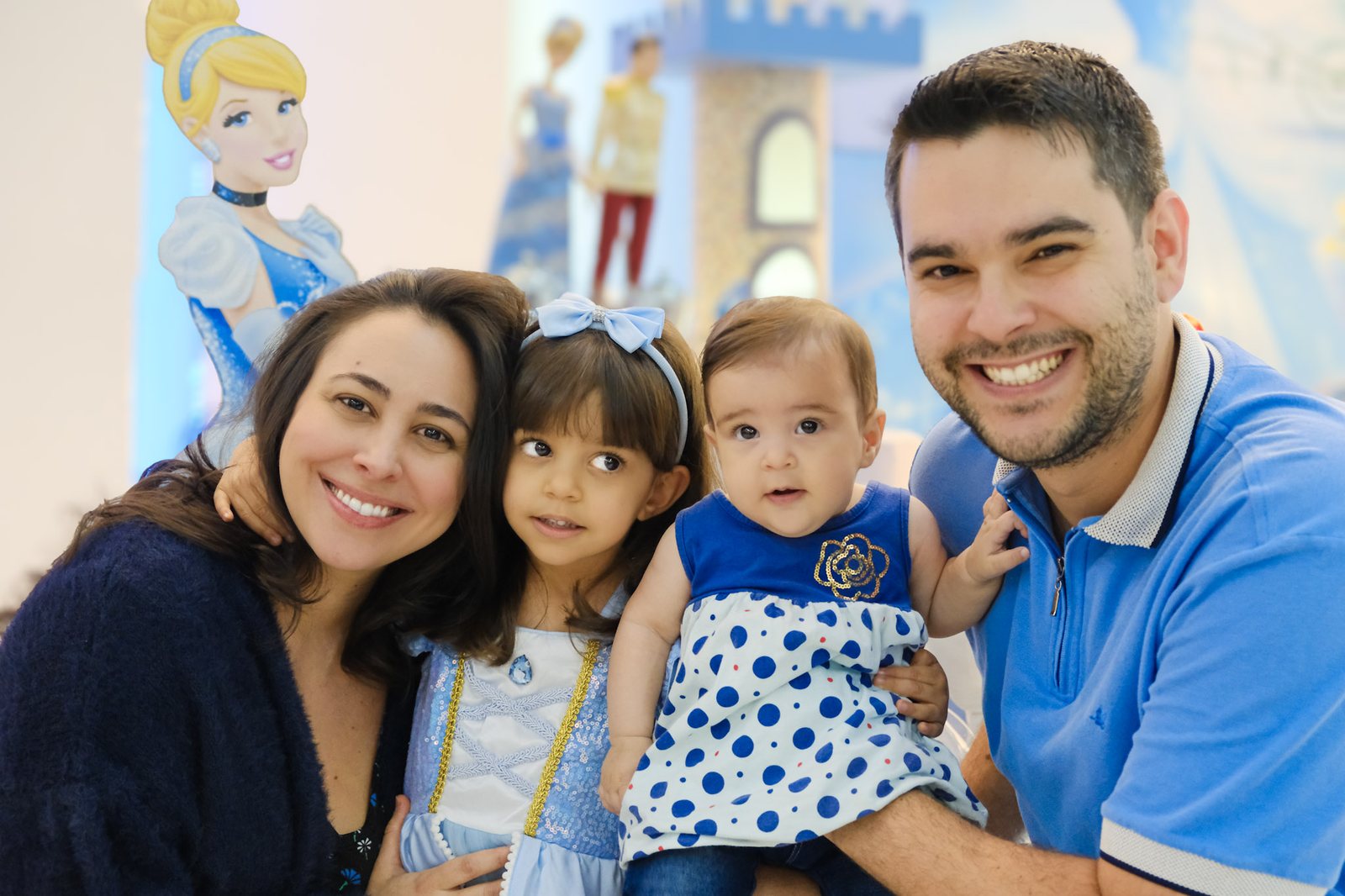Família de pai, mãe e duas filhas sorrindo juntinhas numa festa com tema de Cinderela