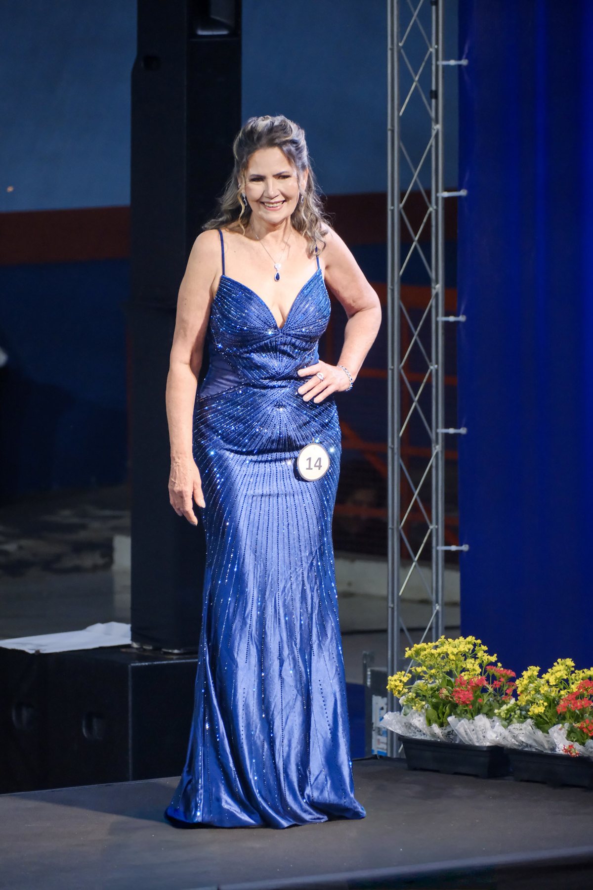 Mulher de vestido longo azul com a mão na cintura, num palco de desfile