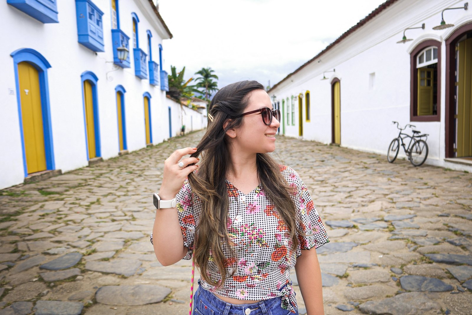 Moça ajeitando o cabelo numa rua de pedra entre casas coloniais coloridas